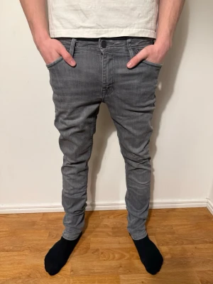 Gråa slim jeans från jack&jones  - Säljer ett par gråa slim jeans med klassisk femficksmodell och dragkedjegylf. Jeansen är i storlek w30 l34 och har en nice passform och är tillverkade i stretchigt denimtyg för extra komfort. Perfekta för en avslappnad och trendig look. Pris kan diskuteras✅