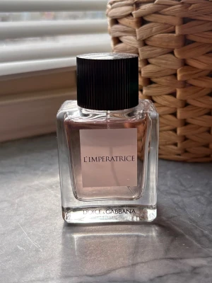 Dolce & Gabbana L'Imperatrice parfym - En elegant parfym från Dolce & Gabbana, L'Imperatrice, i en stilren glasflaska med ljusrosa doftvätska och svart räfflad kork. Flaskan har en modern, fyrkantig form och minimalistisk etikett framtill. 50ml, endast använd enstaka gång 