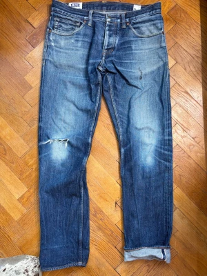 Selvedge jeans från Kings of Indigo - Kings of indigo - Limited selvage. Modellen är ”Clovis Straight fit” .Style name - Clovis Selvage. Wash name - Triple R Japan Dry Selvage.    Storlek 32x32. Bilderna är lite skeva så hör av dig vid behov av fler!  Utgör skick själv ifrån bilderna!  Hör av dig vid frågor!  Öppen för bud  Midja 42cm  Ytterben 100cm  Benöppning 18 cm