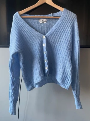 Ljusblå ribbstickad kofta - Supermjuk ljusblå kofta med ribbstickat material och v-ringning. Koftan har långa ärmar, vita knappar framtill och en croppad passform. Perfekt till våren och sommaren! Köpt secondhand och har endast använts några gånger. Liten i storleken❣️