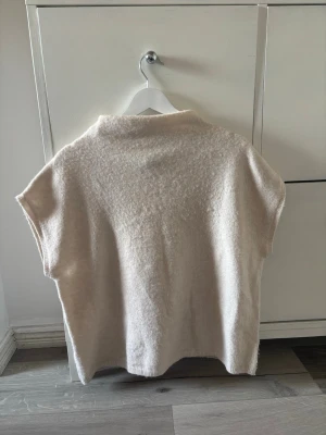 Stickad tröja från Lindex - Säljer en beige stickad tröja med korta ärmar och lös passform. Tröjan har en mjuk, ullig struktur och en enkel design utan synliga detaljer eller mönster. Den är storlek XL men sitter helt okej på mig som är storlek xs. 