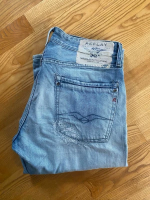 Ljusblå jeans från Replay - Säljer ett par ljusblå jeans från Replay med slitningar och lagade detaljer för en avslappnad och trendig look. Klassisk femficksmodell med raka ben och normal midja. Mycket fint skick!  Modell Rogob. Storlek W 33 L 32