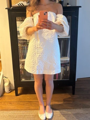 Vit offshoulder klänning - Supersöt vit kort klänning med offshoulder och puffiga trekvartsärmar. Klänningen har en strukturerad, krinklad yta och en avslappnad passform. Perfekt för studenten och sommarens alla tillfällen!