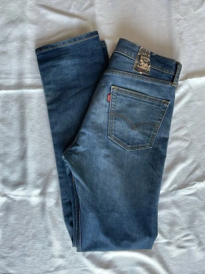 Levi's 513 Jeans blåa - Klassiska blå jeans från Levi's med rak passform och fem fickor. Jeansen har en snygg tvättad look, Levi's ikoniska läderpatch bak i midjan och röd logotagg på bakfickan. Tillverkade i slitstark denim, perfekta för en avslappnad stil. W32 L34. Hör av dig vid funderingar⁉️⚠️Obs! Läderpatchen bak är trasig!