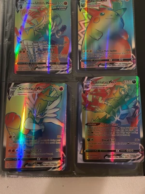 Rainbow VMAX Pokémon kort - Fyra holografiska Pokémon VMAX samlarkort i plastficka: Urshifu VMAX, Pikachu VMAX, Cinderace VMAX och Eternatus VMAX. Kortens framsidor har färgstarka illustrationer och glansig finish. Perfekt för dig som vill utöka din Pokémonkort-samling.