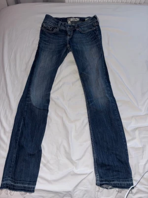 Blå bootcut jeans från BKE denmin  - Snygga blå bootcut jeans från Big Star med slitningar och dekorativa sömmar på bakfickorna. Jeansen har en klassisk femficksmodell och cool tvätt med ljusare partier framtill och bak. Byxorna är uppsprätta längst ner och lite slitna vid uppsprättningen men fortfarande i bra skick.