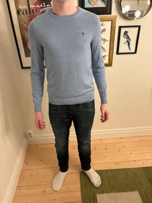 Ljusblå tröja från Morris - Snygg ljusblå rundhalsad tröja från Morris med diskret logga broderad på bröstet. Tröjan har långa ärmar, ribbade muddar och är tillverkad i ett tunt, mjukt material som passar perfekt till jeans. Storlek m men snarare m/s.