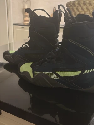 Nike svart/grön boxningssko - Säljer ett par höga boxningsskor från Nike i svart med neongröna detaljer. Skorna har snörning hela vägen upp, meshpaneler för ventilation och en slitstark gummisula med bra grepp. Perfekta för dig som vill ha stilrena och funktionella skor till boxningsträningen. Storlek 43- 44 pris kan diskuteras. 