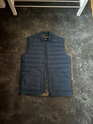 Mörkblå väst från Hampton Republic - Stilren mörkblå dunväst med quiltad design och två stora framfickor. Storlek S hör av er om ni har funderingar 