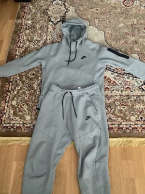  Nike tech fleece tracksuit - Snygga grå Nike tech fleece dress från Nike med svart logga på vänster ben. Byxorna har dragsko i midjan och är tillverkade i mjukt och bekvämt material, perfekta för en avslappnad stil. Klassisk passform med fickor på sidorna.