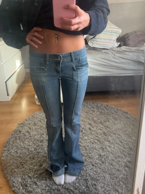 Blå bootcut jeans från NLY Jeans - Säljer ett par ljusblå bootcut jeans från NLY Jeans med låg midja och stora fickor framtill. Jeansen har en klassisk femficksdesign och är tillverkade i denim med snygga sömdetaljer längs benen. Perfekta för en trendig och avslappnad look.