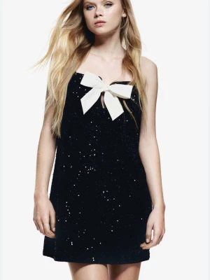 Svart paljettklänning med rosett - Säljer en snygg svart paljettklänning från H&M med en vit rosett framtill. Klänningen är storlek XS och oanvänd. 💞💞 