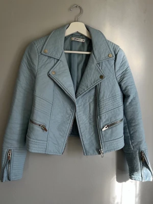 Bikerjacka / skinnjacka ljusblå Gina Tricot storlek 36 - Superfin jacka i pastellblå färg som verkligen höjer vårkänslorna! Perfekt nu till tidiga våren när det fortfarande är lite kyligt ute.   Köpt second hand men aldrig använd av mig då den tyvärr inte passar.  Hittar inga skavanker mer än en pytteliten fläck vid lappen i nacken (se sista bilderna), men det är absolut inget som stör.