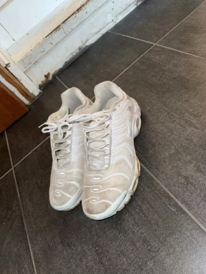 Vita Nike TN - Säljer ett par vita Nike Air Max Plus sneakers med ikoniska vågiga detaljer och synlig dämpning i sulan. Skorna har mesh- och syntetmaterial på ovandelen, samt klassisk snörning. Perfekta för dig som gillar streetwear och sportig stil.1,1 utan kartong