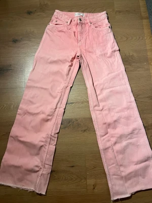 Vida rosa jeans från Mango - Säljer ett par ljusrosa jeans från Mango med vida ben och råa kanter längst ner. Klassisk femficksmodell med knapp och dragkedja framtill. Perfekt för dig som vill ha en cool och färgstark look.