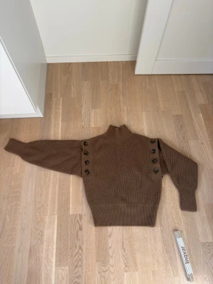  stickad tröja med knappar + väst - Snygg brun/grön/ khaika stickad tröja med hög krage och dekorativa stora knappar längs axlarna. Tröjan har ribbstickad struktur och långa ärmar. Perfekt för dig som gillar en trendig och bekväm look.man kan ta av armarna och ha en fin skjorta under tröjan