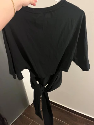 Svart croppad topp med knyt - Snygg svart croppad topp med knyt framtill. Toppen har korta ärmar och rund halsringning. Perfekt att styla med höga jeans eller kjol för en trendig look.