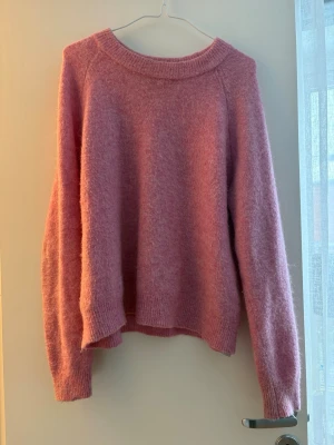 Rosa fluffig stickad tröja - Mysig rosa stickad tröja med rund halsringning och långa ärmar. Tröjan har en lös passform och ribbade muddar vid ärmslut och nederkant. Perfekt för kyliga dagar och enkel att matcha med jeans eller kjol. Tröjan är använd en del, men fortftande mycket fint skick!! Vid snabb affär kan jag tänka mig att sänka priset.