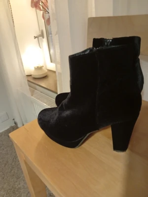 Svarta sammetsstövletter med klack - Snygga svarta stövletter i sammetsmaterial med rund tå och bred klack. Dragkedja på insidan för enkel på- och avtagning. Perfekta för dig som vill ha en stilren och trendig look med lite extra höjd.