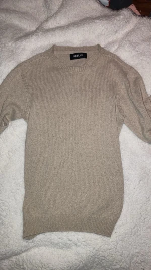Beige stickad tröja från Replay - Snygg beige stickad tröja från Replay med rund halsringning och långa ärmar. Tröjan har en enkel och stilren design med ribbstickade muddar vid ärmslut och nederkant. Perfekt basplagg för lager på lager och passar till det mesta.