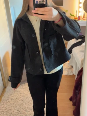 Svart höst/vår jacka med knappar - Storlek M och lite oversized i modellen, går att ha både T-shirt eller hoodies under utan problem, inga tecken på användning då den bara använts max 5 gånger så i nyskick💞Snygg svart jacka med stora knappar framtill och två rejäla fickor. Jackan har en croppad passform och breda slag, perfekt för dig som gillar en stilren och enkel look