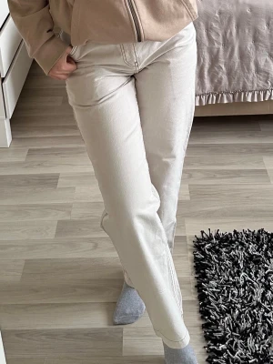 Beige raka cargojeans - Säljer ett par beige cargojeans med raka ben och tydliga kontrastsömmar. Jeansen har klassiska fickor fram och bak samt en extra detaljficka på sidan. Materialet är kraftigt denim och passformen är avslappnad och trendig.