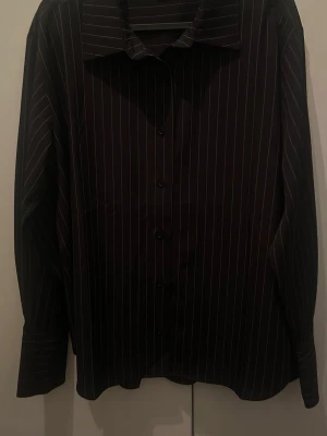 Svart randig skjorta med knappar - Stilren svart skjorta med tunna vita ränder och klassisk krage. Skjortan har lång ärm och knäppning framtill. Gina Tricot🖤🤍