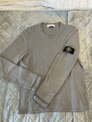 Stone Island tröja/Man - Grå långärmad manströja från Stone Island med klassisk patch på vänster ärm. Tröjan har rund halsringning och diskreta svarta detaljer vid ärmsluten. Tillverkad i ett mjukt material. Passar M/L och priset är diskuterbart