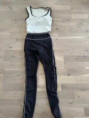 Svart och vitt träningsset linne & tights - Sportigt träningsset med vitt linne med svarta kanter och svarta tights med vita detaljer längs midja och ben. Setet är figurnära och gjort i stretchigt funktionsmaterial, perfekt för gym eller löpning. Inga synliga loggor.