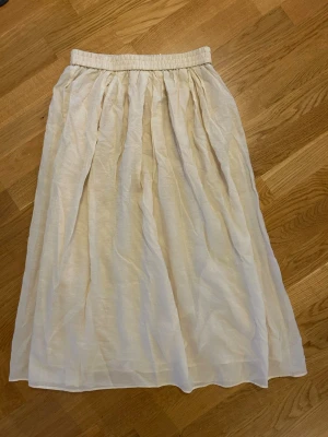 Ny Lång vit kjol med resårmidja - Säljer en lång, luftig vit kjol med resår i midjan. Kjolen har ett skirt, lätt material och faller snyggt med mjuka veck. Perfekt för dig som gillar en enkel men stilren look.
