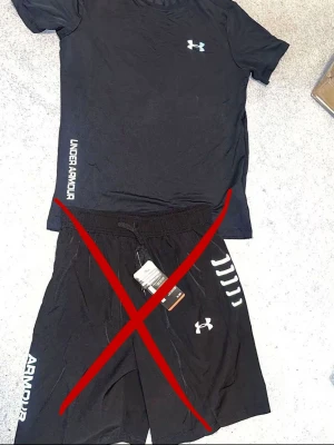 Svart Under Armour t-shirt - Snygg svart t-shirt från Under Armour med logga på bröstet och text längs sidan. T-shirten har korta ärmar och är tillverkad i ett lätt och funktionellt material som passar perfekt till träning.