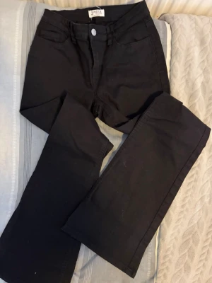 Svarta jeans från Lindex - Säljer ett par svarta jeans från Lindex med klassisk femficksmodell och raka ben. Jeansen har bälteshällor och stängs med knapp och dragkedja. Materialet är mjukt och stretchigt för extra komfort.