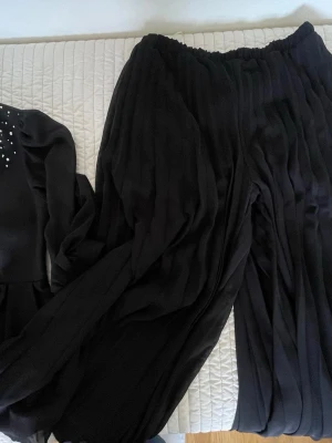 Svarta kavaj set - Säljer en svart blus med långa ärmar och pärldetaljer på axlarna. Blusen har en elegant, lös passform och är tillverkad i ett mjukt, flowy material. Dragkedja bak för enkel påklädning. Perfekt för dig som gillar stilrena och trendiga toppar.