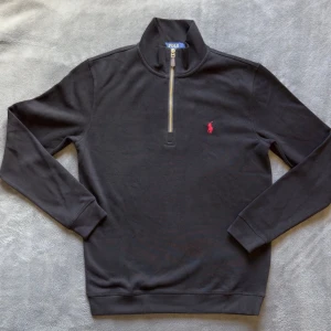 Svart half-zip tröja från Polo Ralph Lauren - Snygg svart långärmad tröja från Polo Ralph Lauren med half-zip och hög krage. Använd endast en gång. Tröjan har det klassiska röda Polo-logot broderat på bröstet och ribbade muddar vid ärmslut och nederkant. Perfekt för en clean och stilren look. Priset kan diskuteras 
