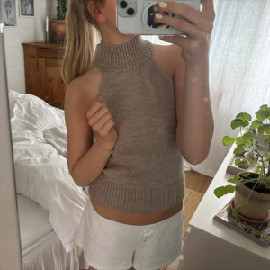 Beige ribbad stickad halterneck topp - Säljer en beige stickad halterneck topp med hög krage och ribbade detaljer. Toppen är ärmlös och croppad, perfekt för en trendig och avslappnad stil. Passar snyggt till både jeans och kjol.
