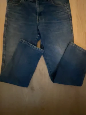 Blå raka jeans med klassisk passform - Säljer ett par blå jeans med raka ben och klassisk femficksdesign. Jeansen har en mörk tvätt och är tillverkade i denim. Perfekta för dig som gillar en enkel och tidlös stil. Riktigt fina!