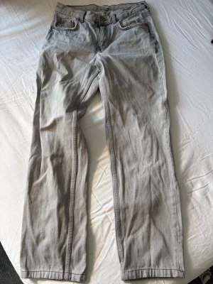 Ljusgrå raka jeans - Säljer ett par ljusgrå jeans med rak passform och klassisk femficksdesign. Jeansen har normal midja och är tillverkade i ett mjukt denimtyg. Perfekta för en avslappnad och stilren look. Små slitningar på vissa ställen men inget som påverkar funktionaliteten på byxorna. Köpare står för frakt. 