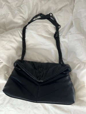 Svart axelväska från Steve madden - Snygg svart axelväska från  Steve Madden med quiltad design och kedjerem. Perfekt för dig som vill ha en trendig och stilren accessoar med lyxig känsla.