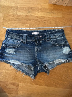 Lågmidjade jeansshorts med slitningar - Gina Tricot - Säljer ett par blåa jeansshorts med slitna detaljer på framsidan från Gina Tricot 14+. OBS! De är i storlek XS, men jag säljer de vidare eftersom jag inte tyckte att storleken alls stämde överens med vad som står på lappen. Dessa var för stora för mig, och jag har XS i andra jeans och jeansshorts från Gina. Därför uppskattar jag storleken som S-M. De två sista bilderna visar hur de sitter på mig för referens.