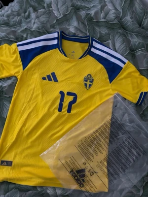 Svenska landslagströja Adidas gul/blå - Säljer en officiell svensk landslagströja från Adidas i gult och blått med nummer 17 på bröstet. Tröjan har klassiska Adidas-ränder på axlarna, rund hals och är tillverkad i ett lätt, ventilerande material. Perfekt för match eller träning!