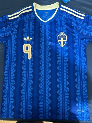 Blå Sverige fotbollströja Adidas - Säljer en blå Sverige fotbollströja från Adidas med gult tryck, nummer 9 och namnet ISAK på ryggen. Tröjan har ett mönstrat tyg, vita ränder på axlarna och broderat landslagsemblem på bröstet. Tillverkad i lätt funktionsmaterial (Climacool). Pris kan diskuteras vid snabb affär.