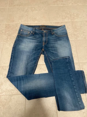 Blå jeans från Nudie Jeans - Säljer ett par klassiska blå jeans från Nudie Jeans med snygg tvätt och slitningar. Modellen har fem fickor, raka ben och kontrastsömmar. Perfekta till en avslappnad stil och tillverkade i bomull för skön känsla. Dom är 100 cm och använda väldigt fåtal gånger (2-3) inga defekter eller liknande. Bara o skriva för fler frågor. Pris kan diskuteras 🤩