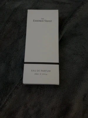 The Essence Vault 499 Eau de Parfum - The Essence Vault 499 Eau de Parfum i en stilren, transparent glasflaska med svartvit etikett. Flaskan rymmer 100 ml och har en modern, rektangulär form. Förpackningen är vit med minimalistisk design och svart detalj. Perfekt för dig som gillar exklusiva dofter. Inspired by Ombre Nomade