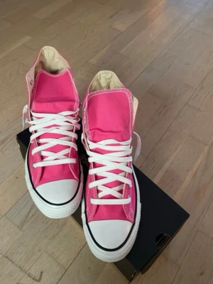 Rosa Converse All Star sneakers  -  Snygga rosa Converse All Star sneakers med klassisk hög modell. Skorna har vit tåhätta i gummi, vita snören och sula. Ovandelen är i canvas och sulan är i gummi. Perfekta för en avslappnad streetstil. De är helt oanvända men ej nyköpta och säljs nu. Original kartongen finns kvar.