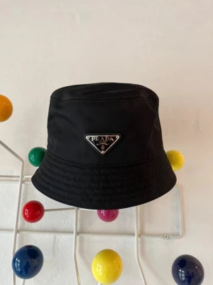 PRADA HATT - Svart "Re-Nylon Bucket Hat" fran PRADA med de Klassiska triangulara logomarket tor dig med klass. *Äkta vara, kvitto medföljer* PRIS KAN DISKUTERAS, tveka ej att skriva vid frågor.