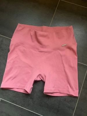 Rosa ribbade cykelshorts Aim'n - Säljer ett par rosa cykelshorts från Aim'n med hög midja och ribbad struktur. Shortsen har en tight passform och är tillverkade i ett stretchigt material som passar perfekt till träning eller chill. Liten metallogo på sidan ger en snygg detalj. Använt fåtal gånger. 