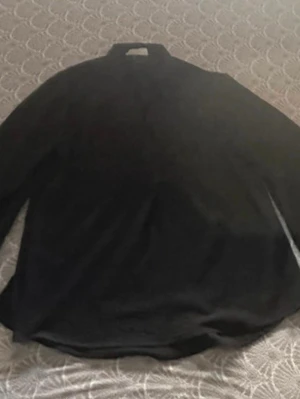 Svart långärmad blus - En stilren svart blus med lång ärm och klassisk krage. Blusen har en rak passform och är tillverkad i ett mjukt, lätt tyg som ger en elegant look. Perfekt att matcha med jeans eller kjol för en trendig outfit.