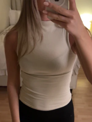 Beige ärmlös ribbad linnetopp - Snygg beige ärmlös linnetopp med ribbad struktur och hög hals. Perfekt att styla med jeans eller kjol för en clean look. Toppen har en tight passform och är superenkel att matcha med andra plagg.