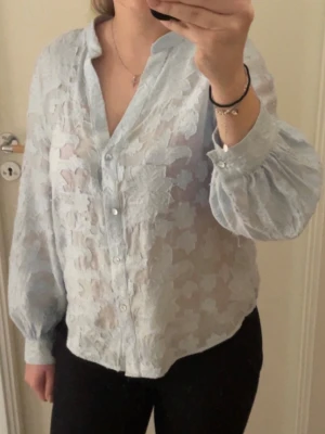 Ljusblå transparent blus med mönster - Säljer en ljusblå blus med tung tyg och blommigt mönster. Den är knappt använd och känner att den är lite liten på mig..💕