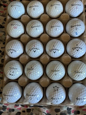Golfbollar från TaylorMade, Callaway, Titleist - Säljer ett set med vita golfbollar från TaylorMade, Callaway och Titleist. Bollarna har olika nummer och logotyper, och ligger i en kartong med plats för 20 bollar. Perfekt för dig som vill fylla på golfväskan inför säsongen.